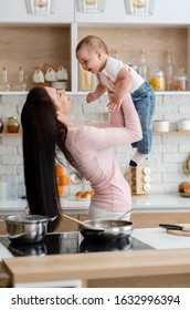 Fun At Kitchen. Mommy Lifting Her Son Up In Air, Cooking Lunch Together