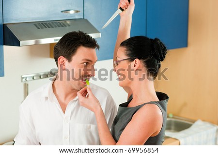 Fun in the kitchen Ã¢Â?Â? woman is holding a knife over the head of her husband
