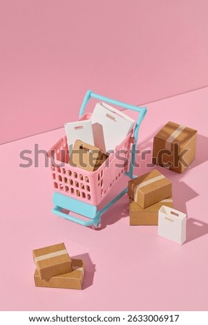 Fun layout of checkout elements like pink shopping carts, shopping bags and cardboard boxes decorated on a pastel pink background. Shopping themed advertising photography