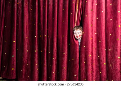 Fun little boy in makeup waiting for his acting cue poking his head out between the curtains as he waits to make his entrance on stage during the performance