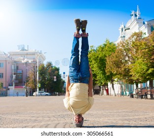 Fun man dancing. Has yellow t-shirt, blue jeans, gray shoes sneakers, slim sport body. Motion on great urban city. Amazing portrait. Sports acrobatic handstand Fitness concept Cool jump Creative quest
