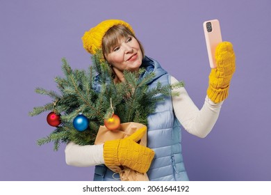 Fun Mature Elderly Lady Woman 55 Years Old Wears Blue Waistcoat Yellow Hat Mittens Holds Spruce Branches Do Selfie On Mobile Cell Phone Isolated On Plain Pastel Light Violet Background Studio Portrait