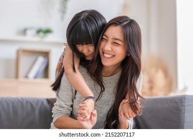 Fun Mom With Cute Baby Girl. Mother And Daughter Playing Together In The Living Room. Asian Girl Embracing Mom From Stand Behind While Mom Sitting On Couch. Happy Family, Motherhood, Childhood Concept