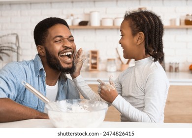 A fun moment captured as an african american father and his daughter have a playful flour fight in the kitchen, symbolizing joy and parenthood - Powered by Shutterstock