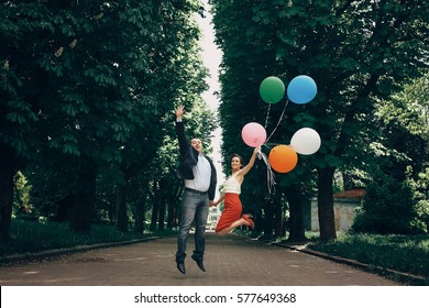 Fun newlywed couple jumping in the air, happy handsome groom and beautiful funny bride jumping with colorful balloons in a park, honeymoon concept. birthday celebration