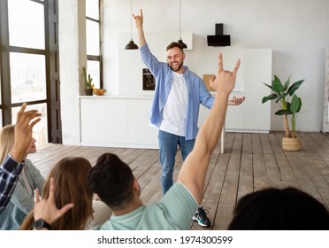 Fun party entertainments concept. Joyful millennial guy playing word guessing game with his diverse friends at home. Group of cheerful millennials enjoying charades or pantomime riddles, indoors