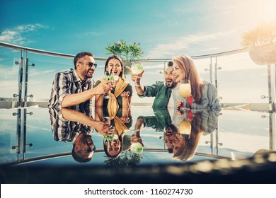 Fun party. Two couples sitting at the table with cocktails and laughing. Beautiful sky, sunlight and plant on background - Powered by Shutterstock