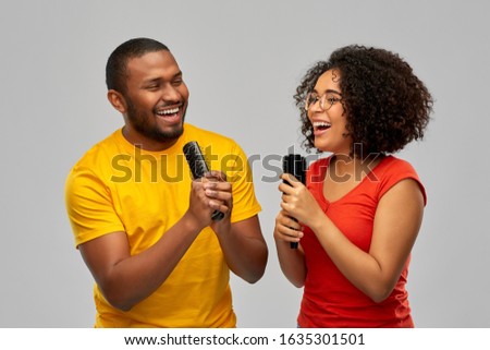 fun and people concept - happy smiling african american couple couple singing to hairbrushes over grey background