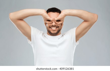 fun and people concept - man making finger glasses over gray background