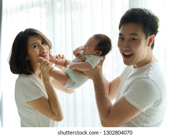 Fun And Play Together. Asian Family, Father And Mother Are Playing With Their Newborn Baby. Dad Holding Baby Body While Mom Holding The Legs And They All Smiling With Happiness.