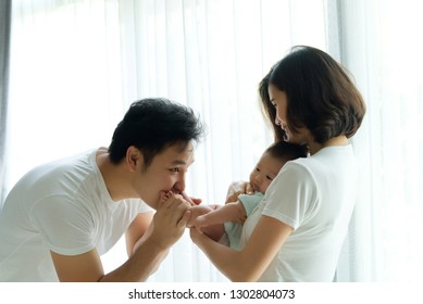 Fun And Play Together. Asian Family, Father And Mother Are Playing With Their Newborn Baby. Mom Holding Baby Body While Dad Holding The Legs And Kissing The Feet. They All Are Smiling With Happiness.