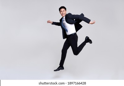 Fun portrait of happy energetic young Asian businessman jumping in mid-air isolated on studio white background.