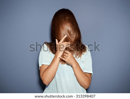 Fun portrait of a woman hiding behind her long brown hair as she pulls it down over her face with her hands, upper body over grey