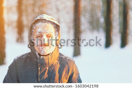 Fun portrait of an young frozen man. Jogging in a blizzard in the woods. Face covered with snow and frost. Closeup portrait of happy young guy smiles in cold weather in the winter forest at sunset