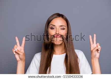 Fun prank joy entertainment concept.  Close up portrait of  young charming brunette shows v-sign and holds her hair over her lip like a fake mustache isolated on gray background