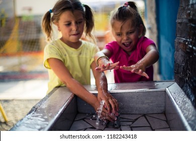  Fun and refreshment in summer day. Two little girls playing with water in playground. Close up.