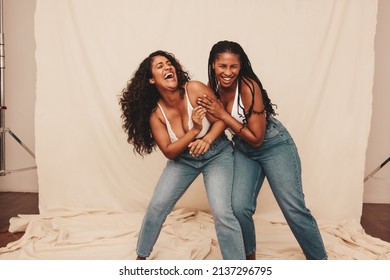 Fun in the studio. Two cheerful young women laughing and being playful while wearing denim jeans against a studio background. Two happy female friends being their natural selves.