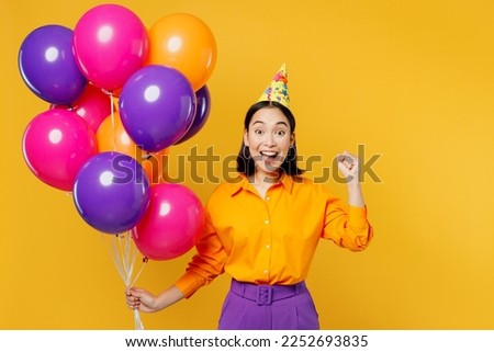 Fun surprised shocked young woman wears casual clothes hat celebrating hold bunch of colorful air balloons do winner gesture isolated on plain yellow background. Birthday 8 14 holiday party concept