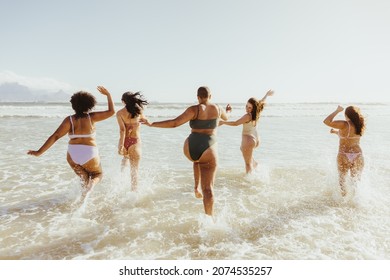 Fun in swimwear. rearview of a group of cheerful female friends splashing water while running together at the beach. Group of carefree young women having fun and enjoying their summer vacation.