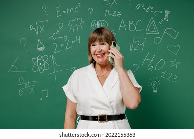 Fun Teacher Mature Elderly Senior Lady Woman 55 Wear White Shirt Look Aside Talk Speak On Mobile Cell Phone Conducting Pleasant Conversation Isolated On Green Wall Chalk Blackboard Background Studio