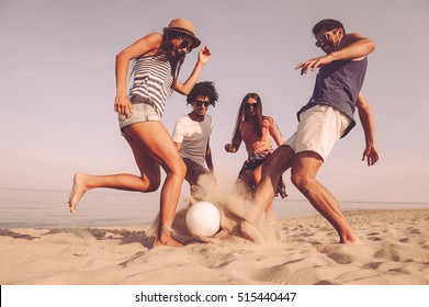 Fun time with friends. Group of cheerful young people playing with soccer ball on the beach - Powered by Shutterstock