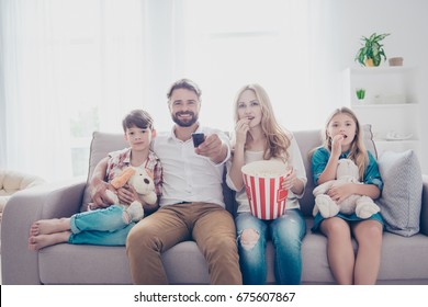 Fun time together. Happy family of four is watching interesting educational documentary, eating popcorn, at home on a couch