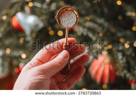 Fun tin casting set for New Years party.hand holding a spoon with a pewter coin inscribed Happy New Year on a Christmas tree backdrop. Fortune telling with melting tin 