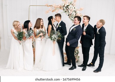 Fun Wedding Group Photo. Bride And Groom Kiss, Bridesmaids And Best Men Glance And Laugh