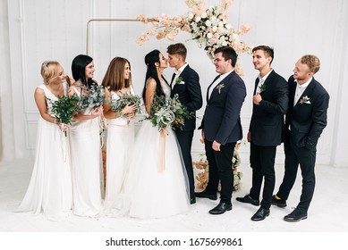 Fun Wedding Group Photo. Bride And Groom Kiss, Bridesmaids And Best Men Glance And Laugh