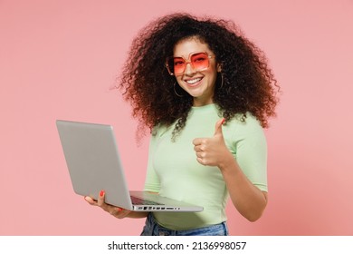 Fun Young Curly Latin Woman 20s Years Old Wears Mint T-shirt Sunglasses Hold Use Work On Laptop Pc Computer Showing Thumb Up Like Gesture Isolated On Plain Pastel Light Pink Background Studio Portrait