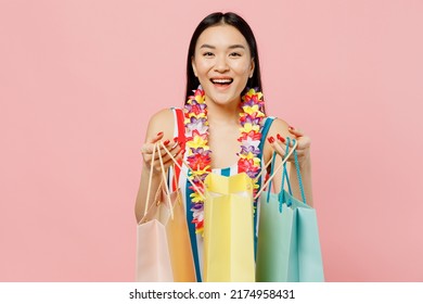 Fun young happy woman of Asian ethnicity in striped swimsuit hawaii lei hold show package bags with purchases after shopping isolated on plain pastel pink background. Summer vacation sea rest concept