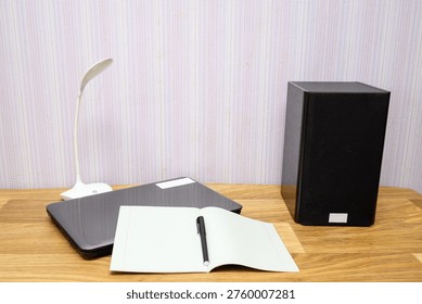 functional area for study or work featuring a closed grey laptop, acoustic system, white led lamp and paper notebook with a pen on a table top with natural wooden texture for productivity