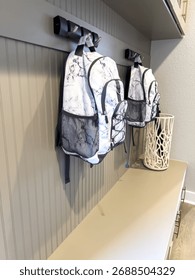 A functional entryway space with mounted wall hooks holding two patterned backpacks. The wall paneling and bench area below add texture and utility to the design.