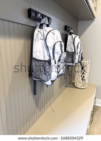 A functional entryway space with mounted wall hooks holding two patterned backpacks. The wall paneling and bench area below add texture and utility to the design.