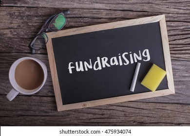 Fundraising On Blackboard With Cup Of Coffee, With Glasses On Wooden Background