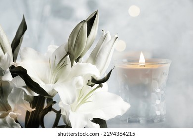 Funeral. Beautiful lilies and burning candle on light blurred background, bokeh effect. - Shutterstock ID 2294364215