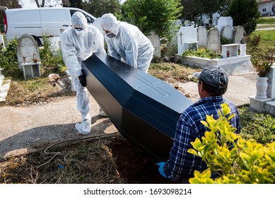 Funeral Home Employees Wear Protective Suits To Protect Themselves From Coronavirus, As They Put A Coffin Inside A Grave.