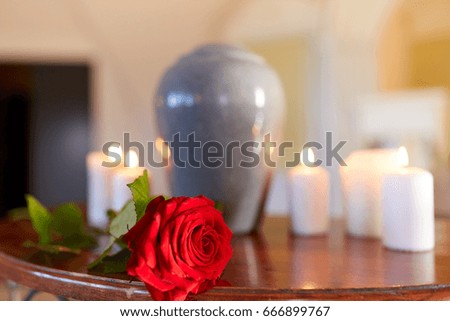 funeral and mourning concept - red rose and cremation urn with burning candles on table in church