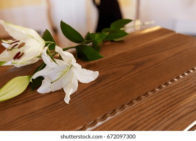 Funeral And Mourning Concept - White Lily Flower On Wooden Coffin Lid At Funeral In Church