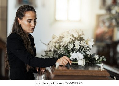 Funeral, sad and woman with flower on coffin after loss of a loved one, family or friend. Grief, death and young female putting a rose on casket in church with sadness, depression and mourning - Shutterstock ID 2225083801