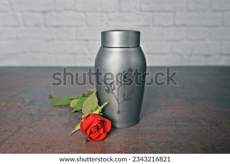Funeral urn beside a red rose. Horizontal image with selective focus.