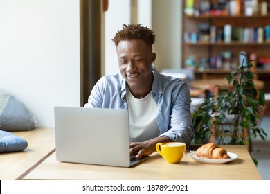 Funky Black Guy Using Laptop Computer For Online Work Or Studies At Cozy City Cafe. Industrious Young Student Having Web Conference Or Remote Lesson On PC At Coffee Shopt