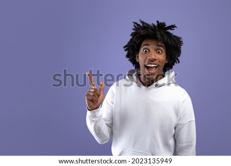 Funky black teen guy experiencing AHA moment, having creative idea, pointing up on violet studio background, copy space. Attractive African American teenager gesturing eureka