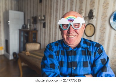 Funky Smiley Caucasian Retired Senior Man In A Flannel Shirt Looking At Camera, And Smiling With Rainbow Glasses. LGBT Supporter. Vintage Interior. High Quality Photo