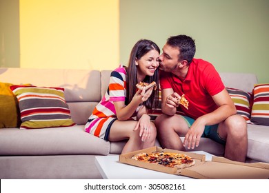 Funky Young Couple Eating Pizza On A Couch In Front Of A Green Wall