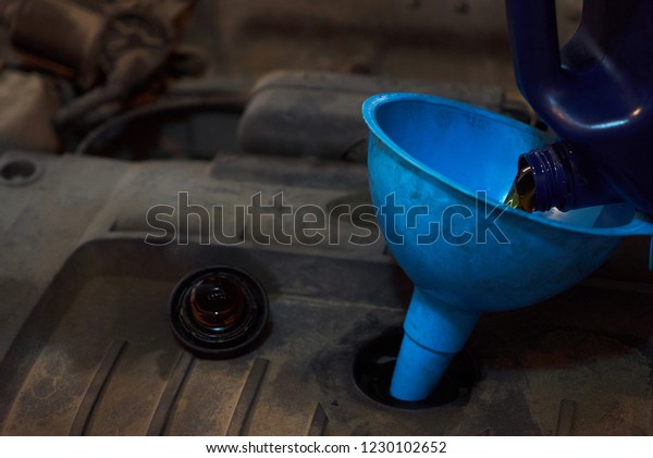 Funnel pouring oil to car engine , close up.\
Change the car oil in garage\
service