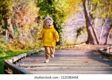 Funny 3 years boy wearing yellow bright rain coat screaming and running on wood path walk in sunny autumn forest