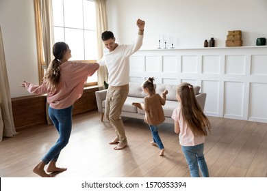 Funny Active Family Of Four Young Adult Parents And Cute Small Children Daughters Dancing Together In Living Room Interior, Carefree Little Kids With Mum Dad Having Fun Laughing Enjoy Leisure At Home