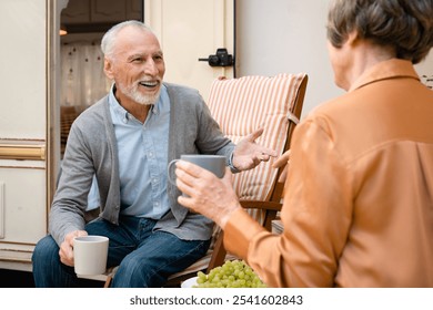 Funny active seniors talking, drinking hot beverage during holidays in caravanning driving trailer motor home. Eco-tourism, away from everything - Powered by Shutterstock