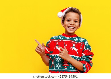 funny african american boy in christmas clothes points with his hands to the side on yellow isolated background, 9 year old child in santa hat shows and advertises copy space - Powered by Shutterstock